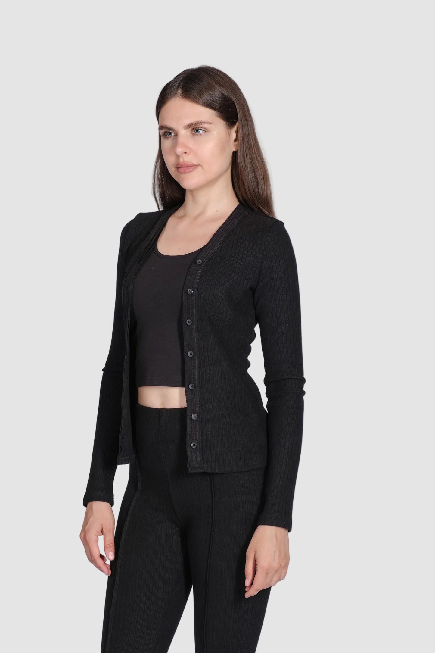 Woman wearing a black cardigan over a black top and pants on a white background