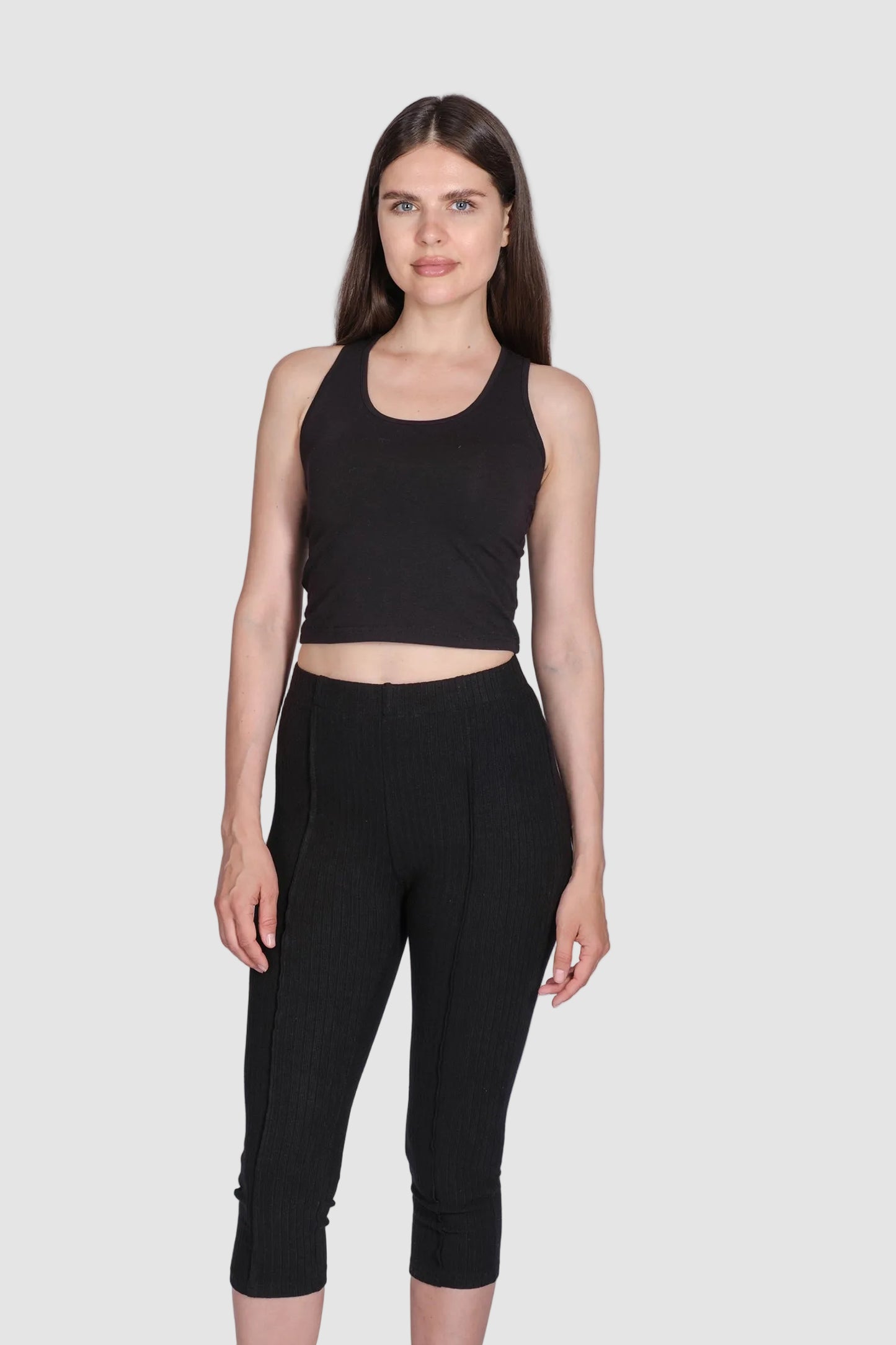 Woman wearing a black sleeveless top and capri leggings on a white background
