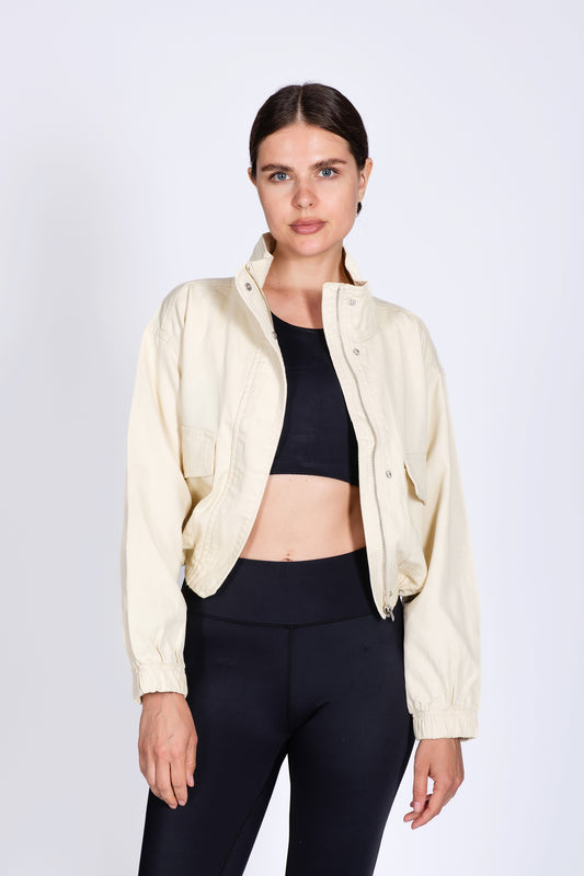 Woman wearing a cream jacket over a black top and pants on a white background