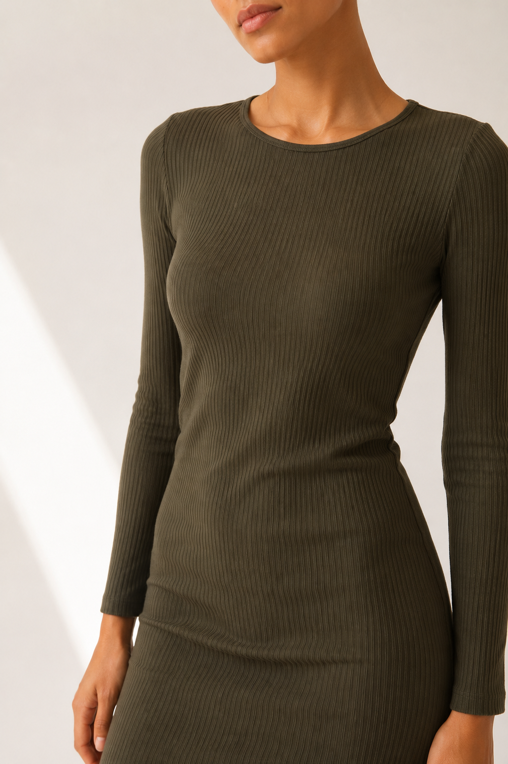 A woman wearing a ribbed long-sleeve crewneck dress in olive green, shown from the chin down against a light neutral background.