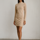 Woman wearing a beige long-sleeve dress against a plain background