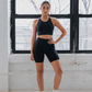 Woman in black athletic wear standing in a room with large windows.