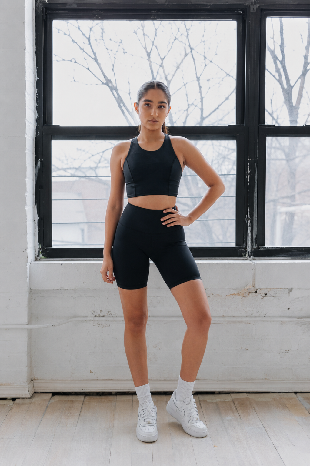 Woman in black athletic wear standing in a room with large windows.