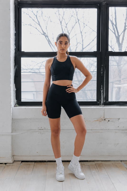 Woman in black athletic wear standing in a room with large windows.
