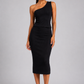A woman modeling a black one-shoulder midi dress with a peplum waist, paired with white strappy sandals, against a solid gray studio background.