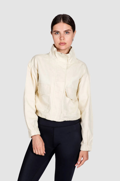 Woman wearing a cream-colored jacket and black pants on a white background