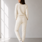Person wearing a cream-colored outfit standing in a minimalistic room with a large window.