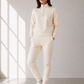 Model with half zip sweatsuit in cream against a beige wall.