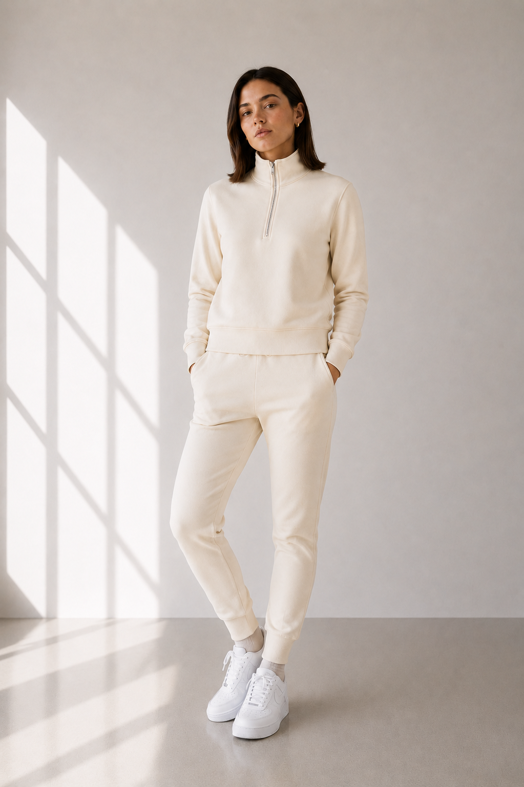 Model with half zip sweatsuit in cream against a beige wall.