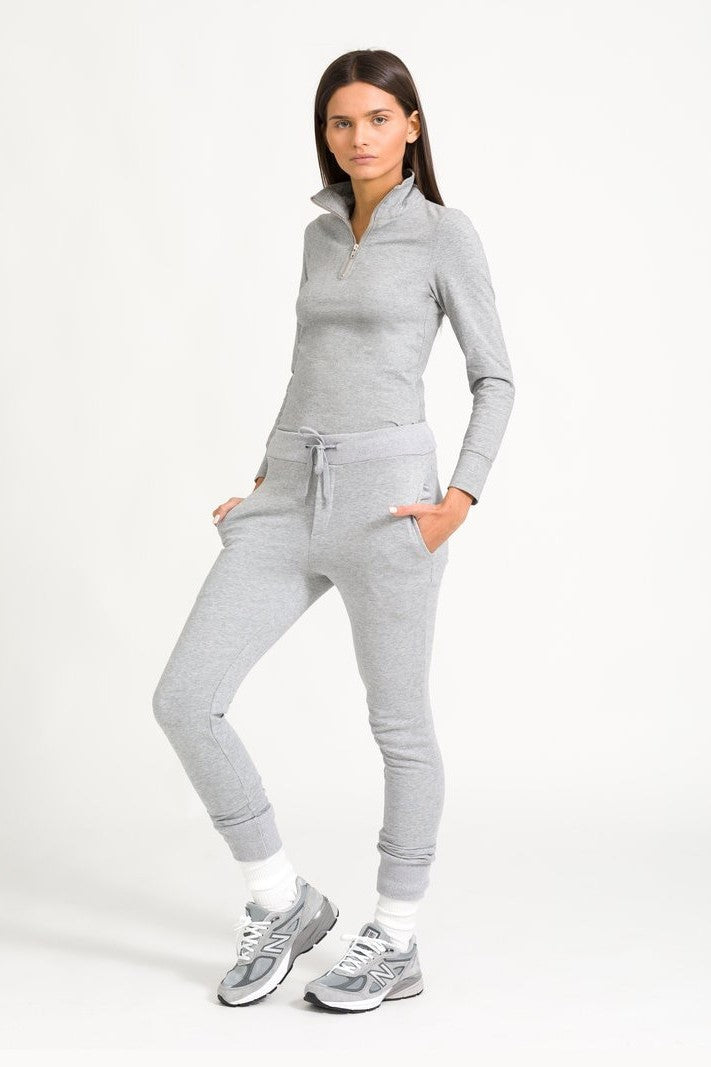 A model wearing a gray half zip top with a silver zip fastening, paired with matching pants and white sneakers.