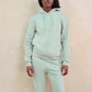 Person wearing a light green hoodie and pants against a beige background