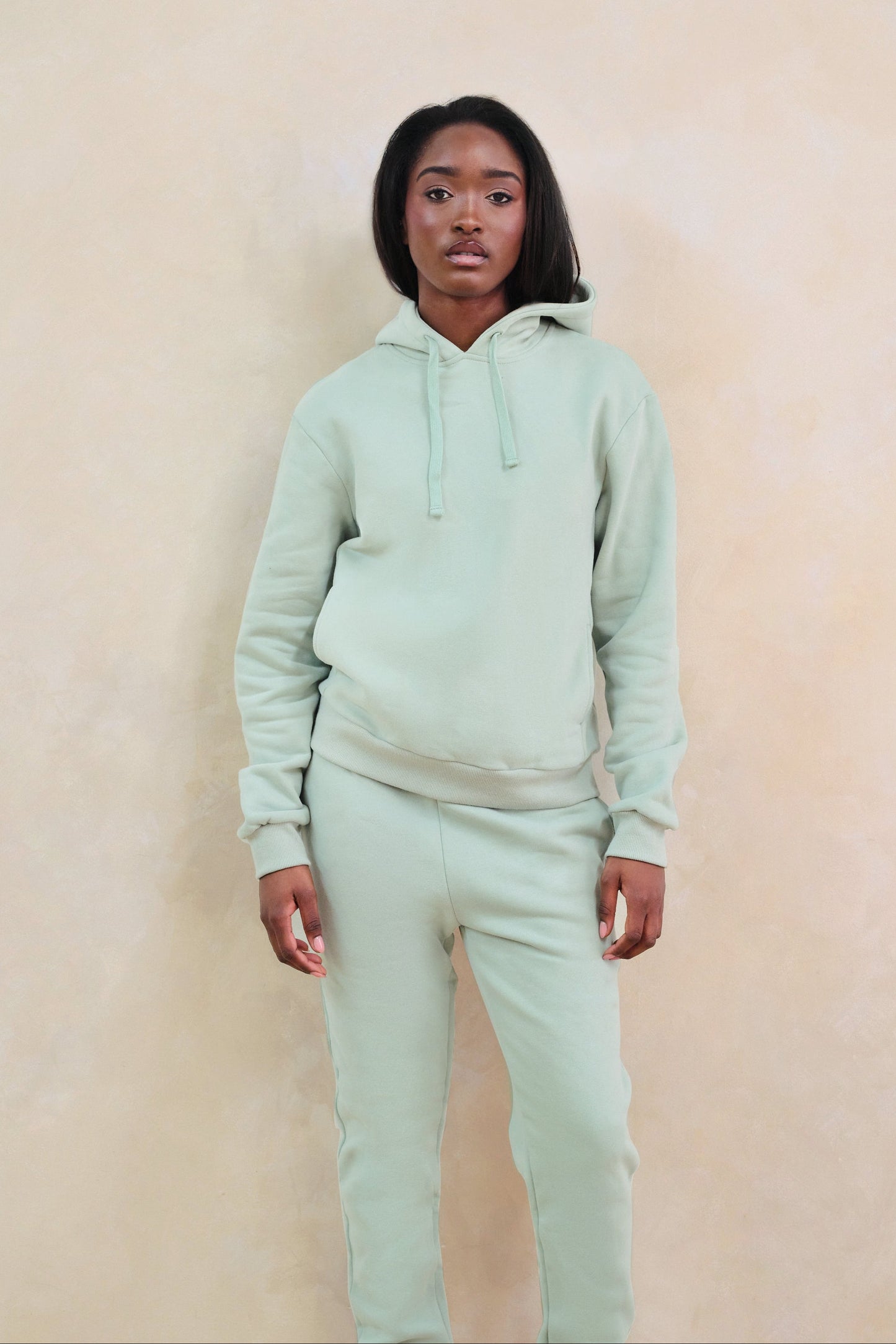 Person wearing a light green hoodie and pants against a beige background