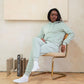 Person wearing a light green tracksuit sitting on a chair in a minimalistic room.