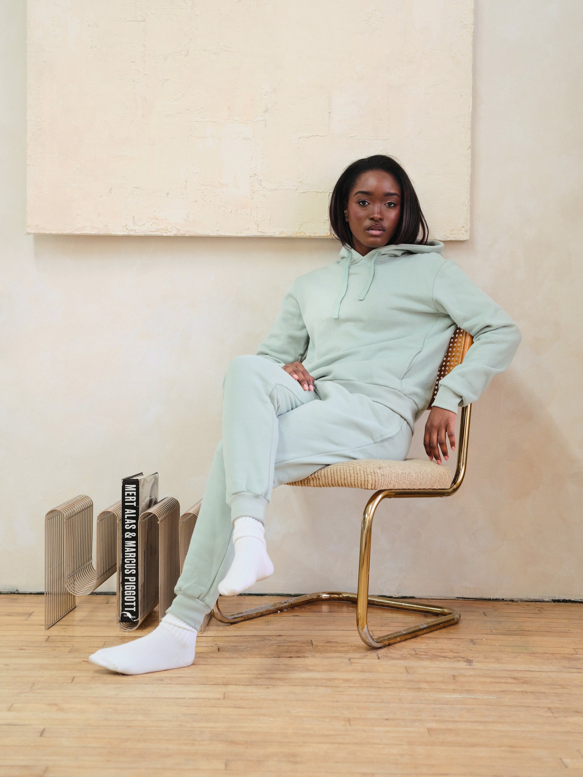 Person wearing a light green tracksuit sitting on a chair in a minimalistic room.