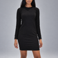 A woman modeling a black long-sleeve crewneck mini dress against a solid gray studio background.