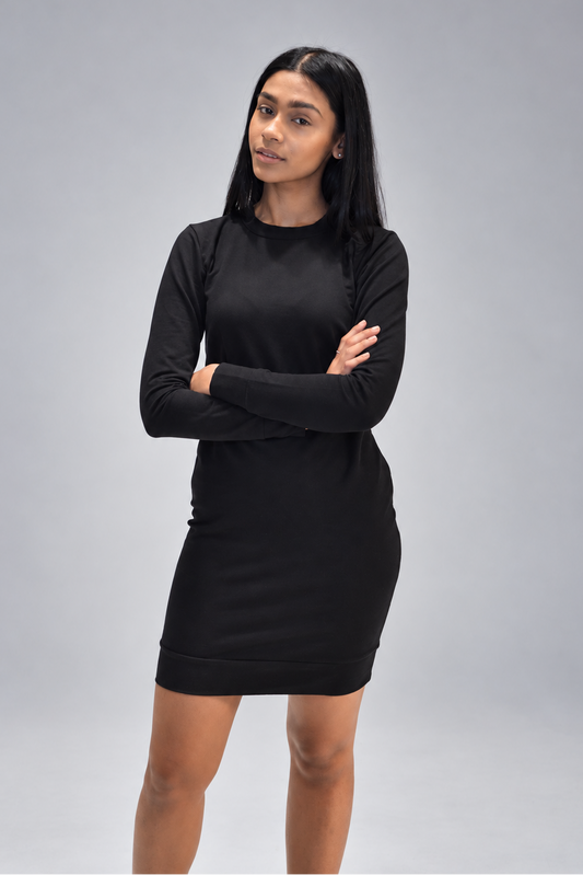 A woman modeling a black long-sleeve mini dress with a crew neck, standing against a neutral gray studio background with her arms crossed.