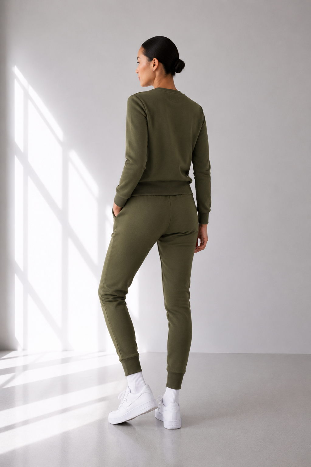 Person wearing an olive green tracksuit standing in a well-lit room with a window.