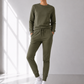Person wearing a green tracksuit standing in a bright room with large windows.