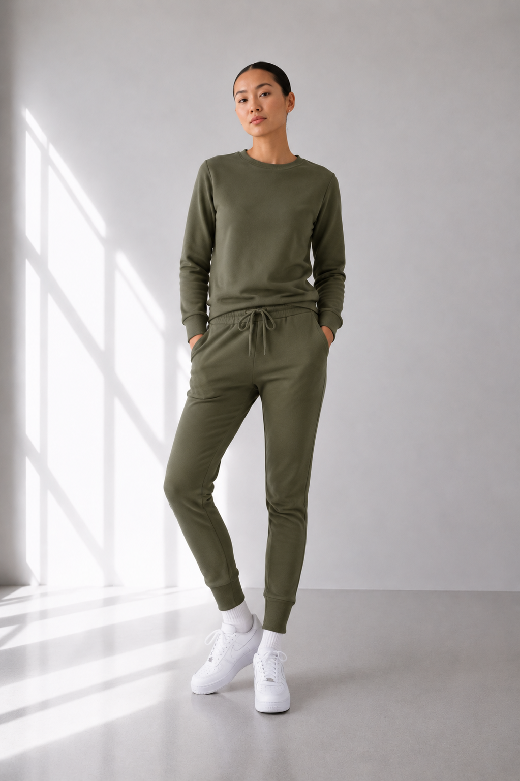 Person wearing a green tracksuit standing in a bright room with large windows.