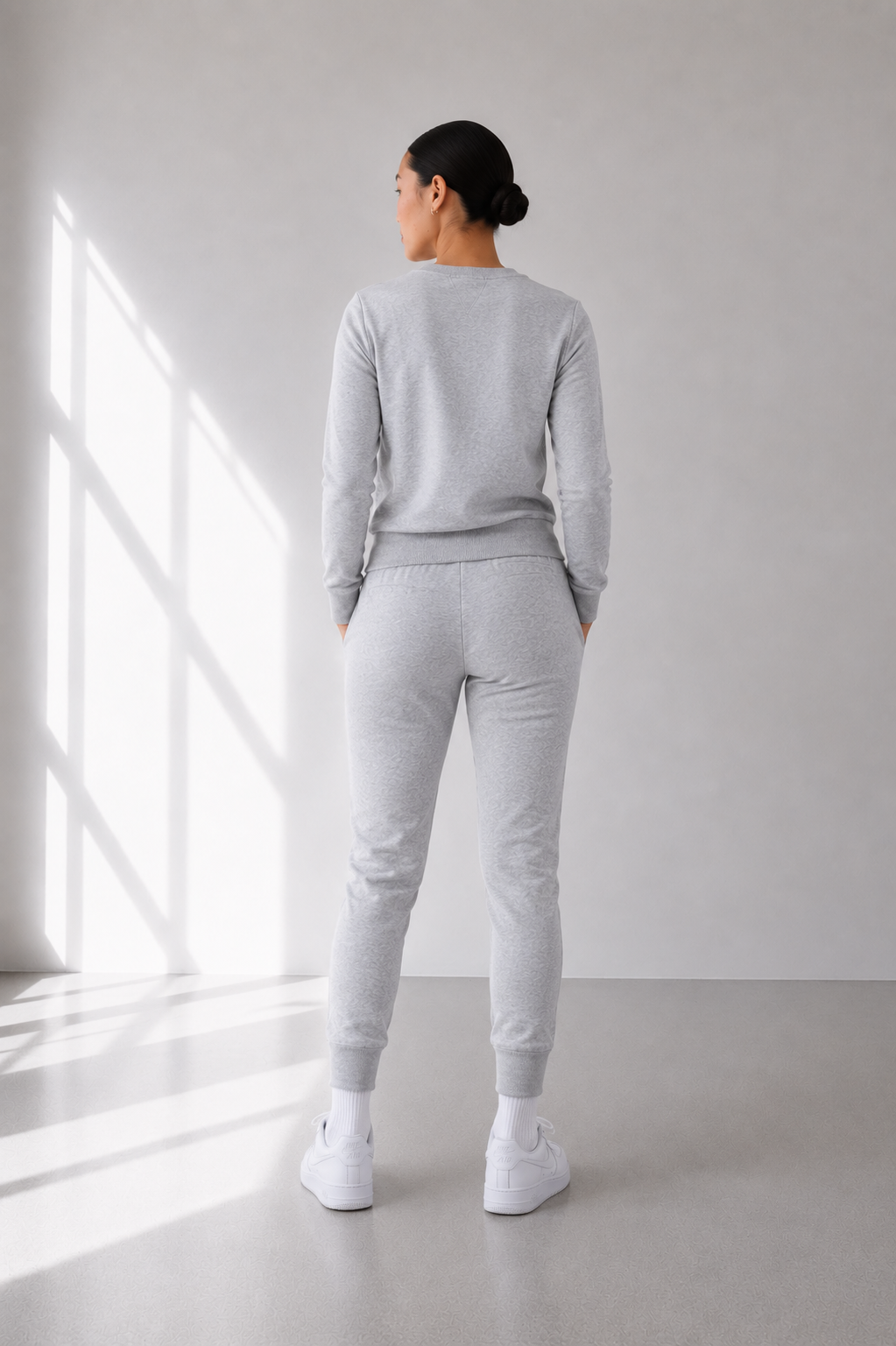 Person wearing a gray tracksuit standing in a well-lit room with a window.