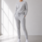 Person wearing a gray tracksuit standing in a bright room with sunlight streaming in.