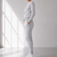 Person wearing a light gray outfit standing in a minimalistic room with a large window.