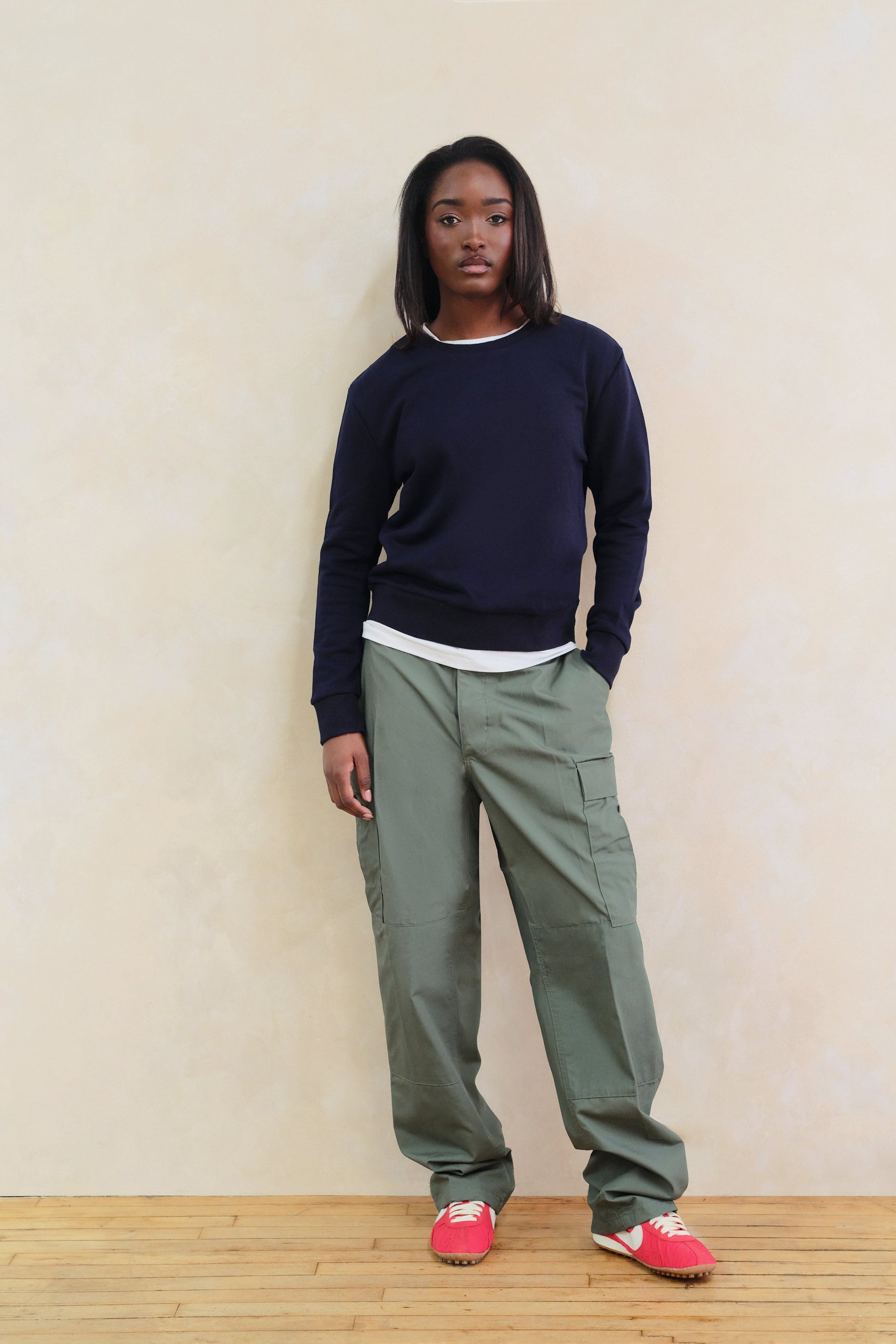 Person wearing a navy sweater and green cargo pants against a beige wall.