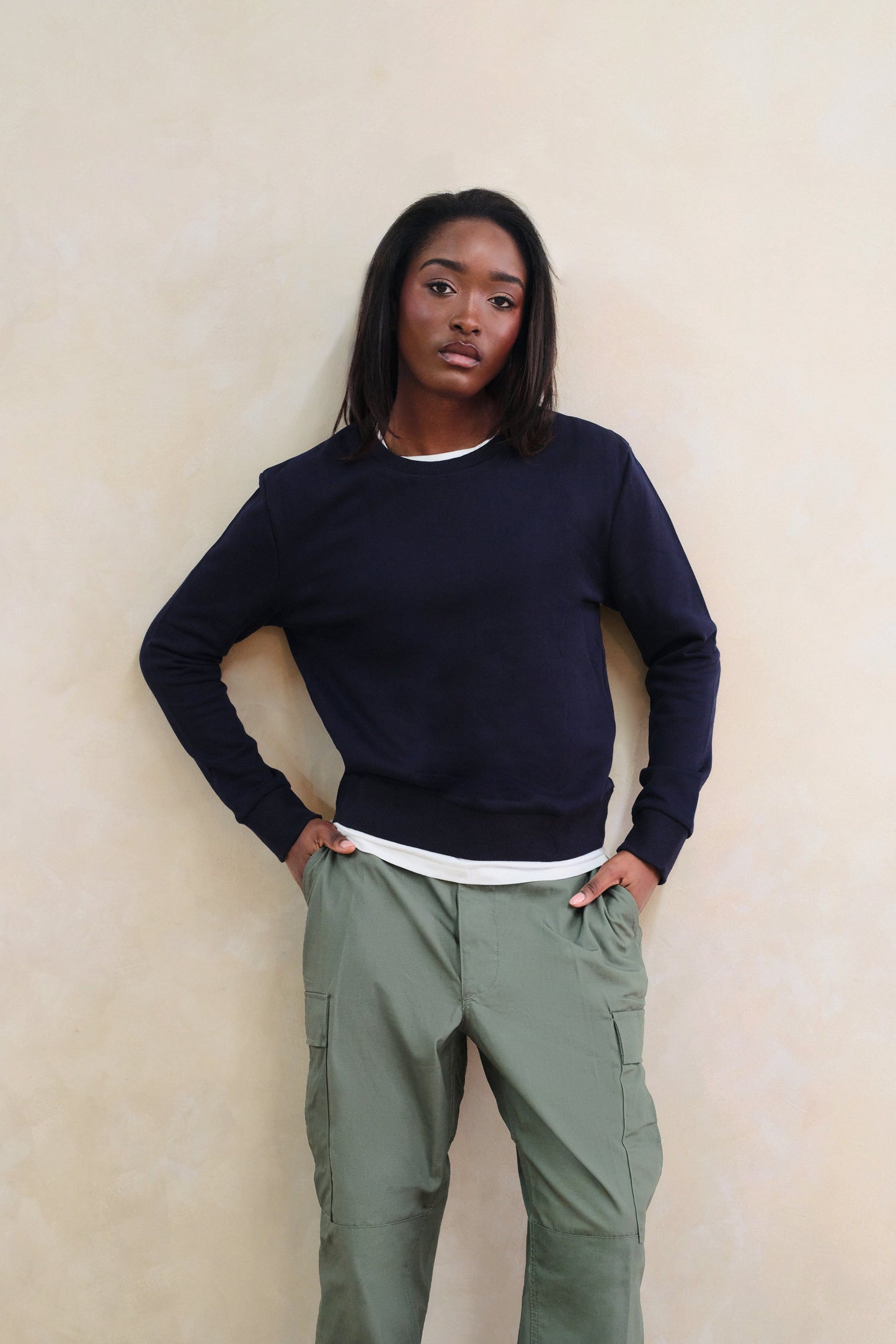 Person wearing a navy sweater and green cargo pants against a beige wall