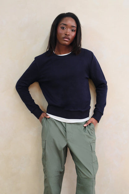 Person wearing a navy sweater and green cargo pants against a beige wall