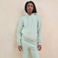 Person wearing a light green hoodie and pants against a beige background
