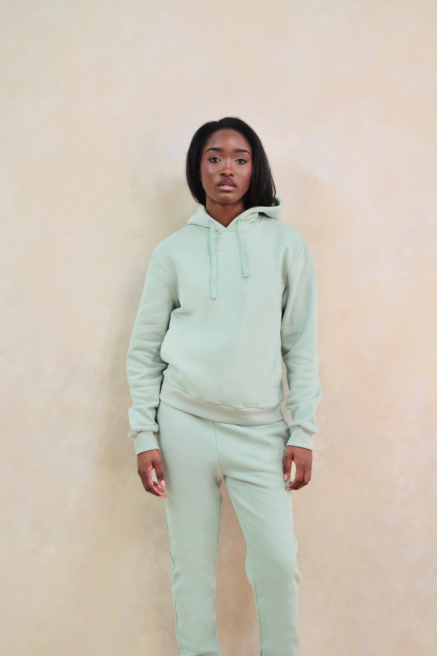 Person wearing a light green hoodie and pants against a beige background