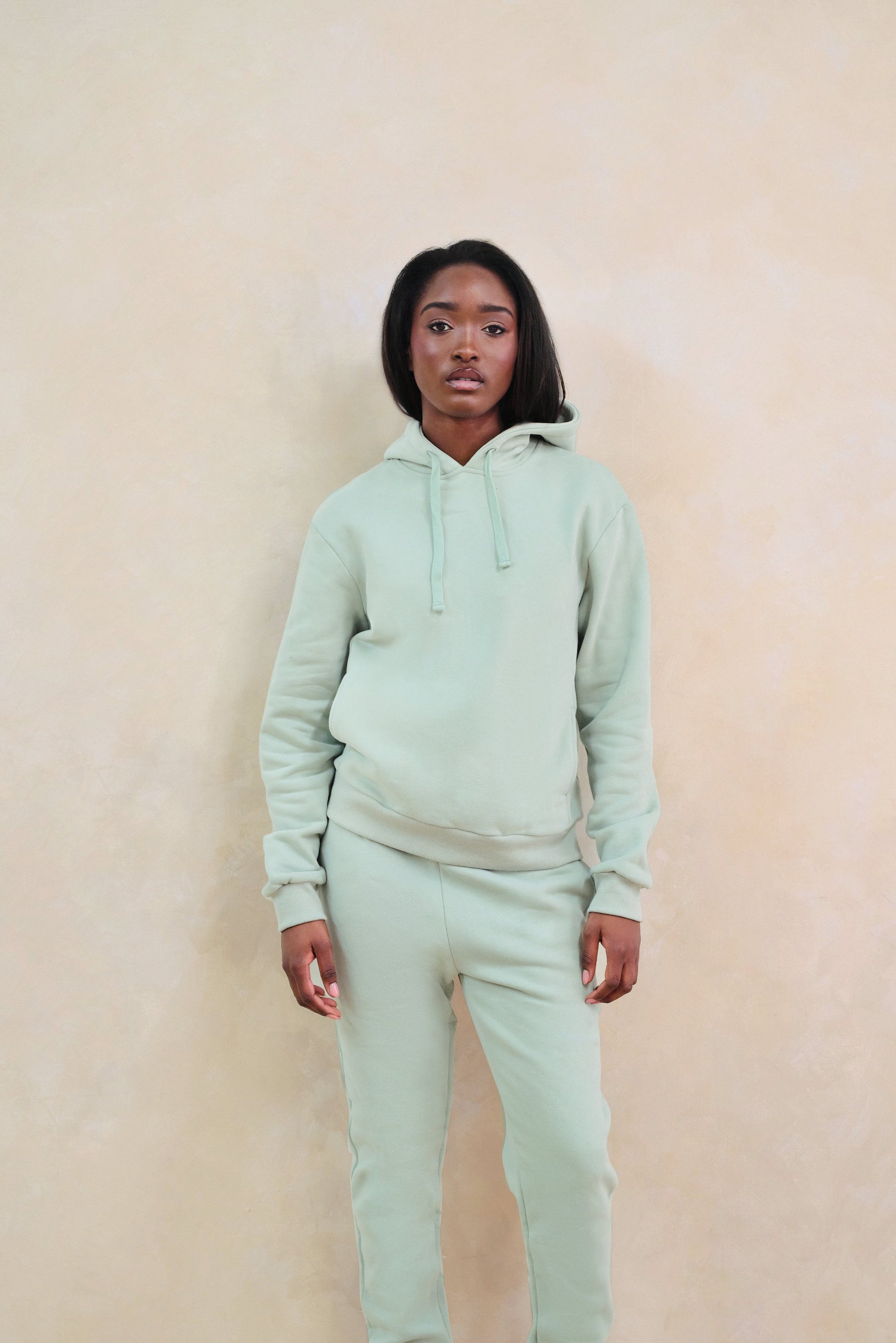 Person wearing a light green hoodie and pants against a beige background