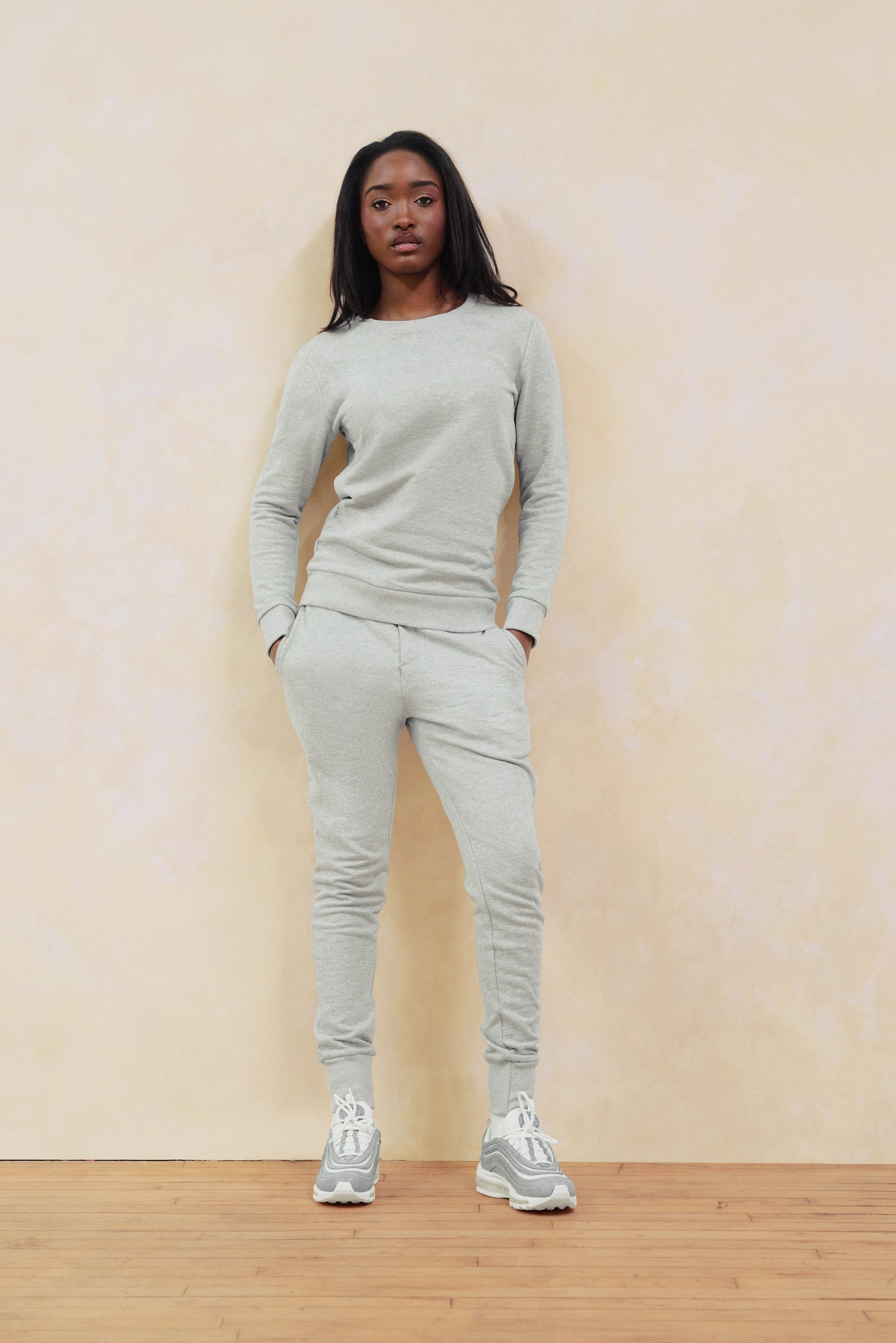 Person wearing a light gray outfit standing against a plain wall.