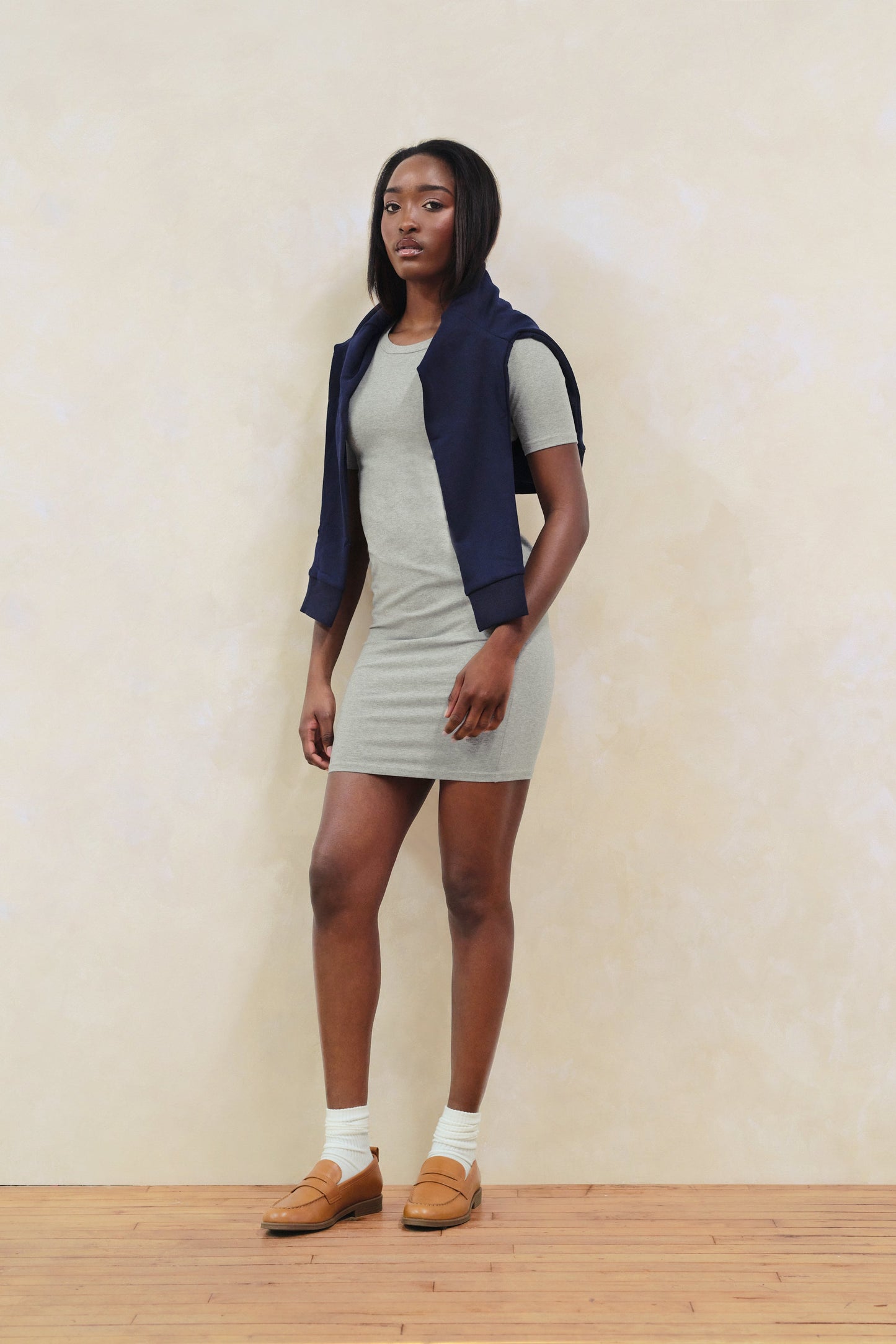 Woman wearing a gray dress with a navy vest against a plain background