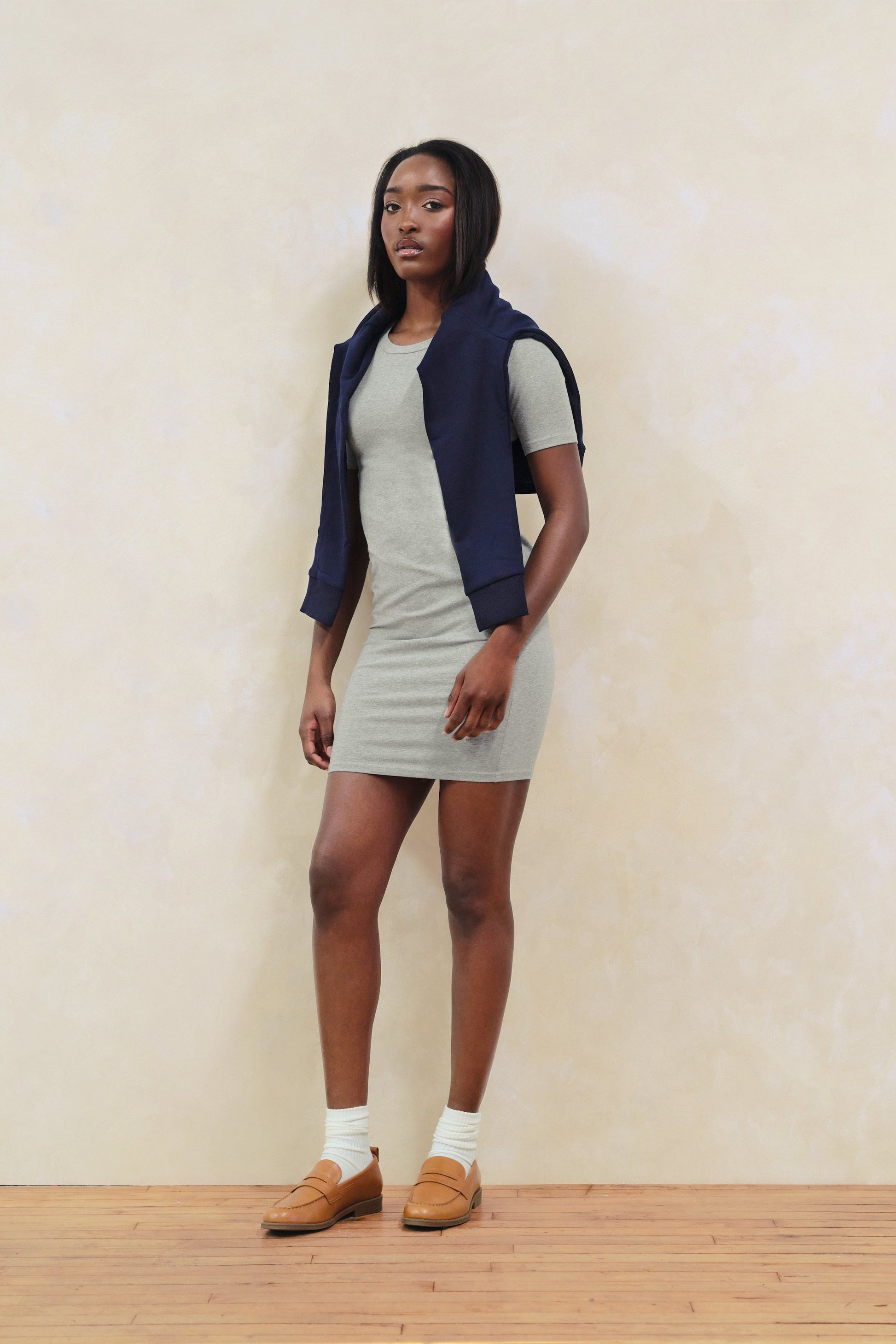 Woman wearing a gray dress with a navy vest against a plain background