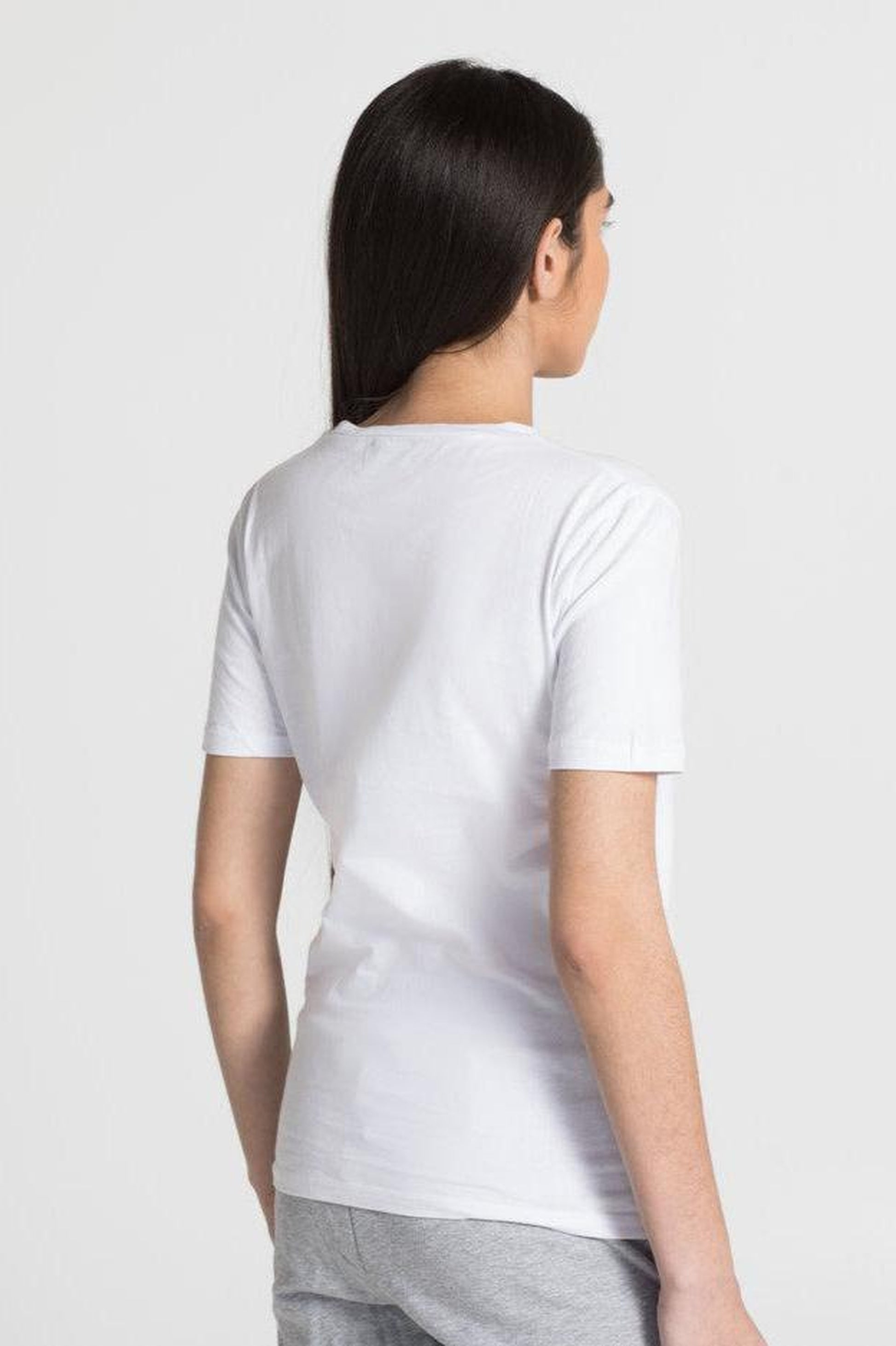 A woman shown from the back wearing a plain white short-sleeve crewneck t-shirt and light gray sweatpants, set against a solid light gray studio background.